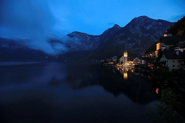 The alpine village of Hallstatt glows at dusk on the banks of Hallstaettersee lake in